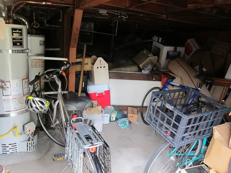 A cluttered basement storage area with bicycles, crates, a cooler and boxes next to a water heater