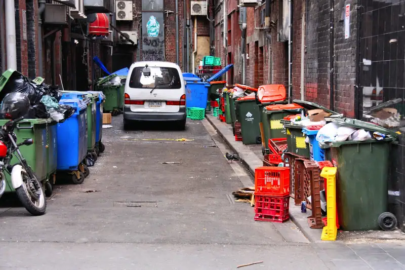 A city service alley lined with overflowing commercial wheelie bins and recycling containers